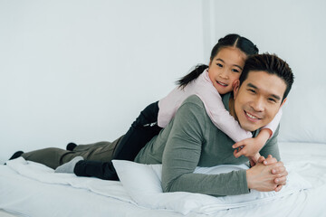 Cheerful Asian girl lying on father's back looking at camera
