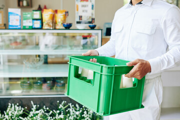 Cropped image of delivery man in white uniform carrying plastic milk crate to the grocery store