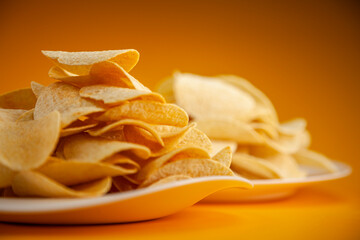 Potato chips on white plate close-up against yellow background