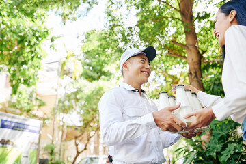Happy smiling Vietnamese delivery man giving set of milk bottles to pretty young woman