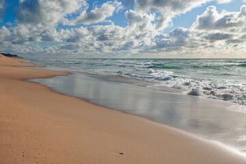 Beautiful seascape. Sandy beach, stormy sea, and cloudy sky on background