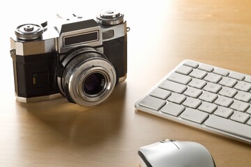 Retro analog SLR camera next to computer keyboard and mouse on wooden desk in office, digital...