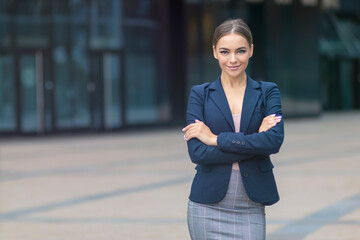 Happy positive young businesswoman in formal suit standing outdoors business centre with her hands,...