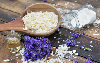 Obraz na płótnie Canvas spoon full of flakes of soap with essential oil and bunch od lavender flowers and sodium bicarbonate on wooden background