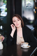 pensive or thoughtful woman sitting at table in cafe wearing black jacket - 368936306