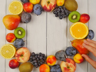 a woman's hand And frame of ripe various fruits on a white background of boards. Close-up. Proper nutrition. Space for text.