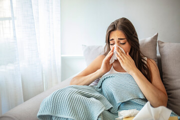 Sick Woman Covered With a Blanket Lying in Bed With High Fever and a Flu, Resting at Living Room. She Is Exhausted and Suffering From Flu. Sick Woman With Runny Nose Lying in Bed.