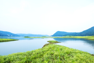 Peaceful and beautiful lake and green field background blue sky,early summer morning landscape.