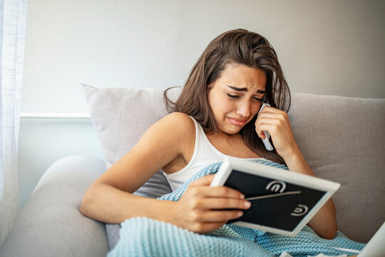 Depressed young woman crying, holding boyfriend or husband picture close up, stressed upset girl suffering from break up or divorce, sitting on couch at home alone, feeling lonely and hopeless