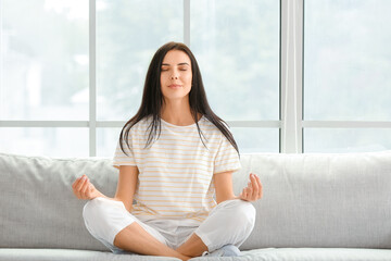 Young woman meditating on sofa at home