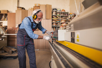 Side view of a senior carpenter using an edgebanding machine