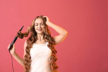 Beautiful young woman with curling iron for hair against color background