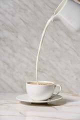 Pouring of milk in cup of tasty coffee on table