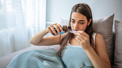 Sick woman sitting at the window of the house and drink the bitter medicine. Girl drinks a...