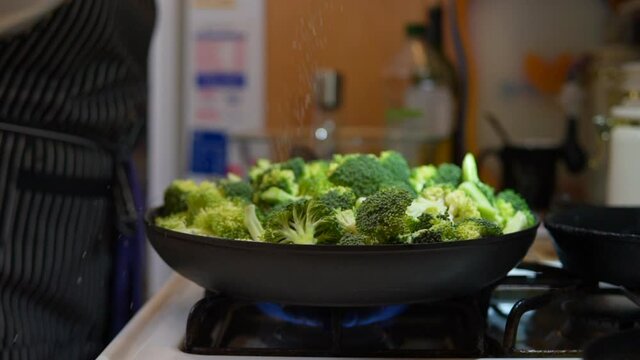 Sprinkling salt on a skillet full of broccoli as it cooks on the stove top - slow motion