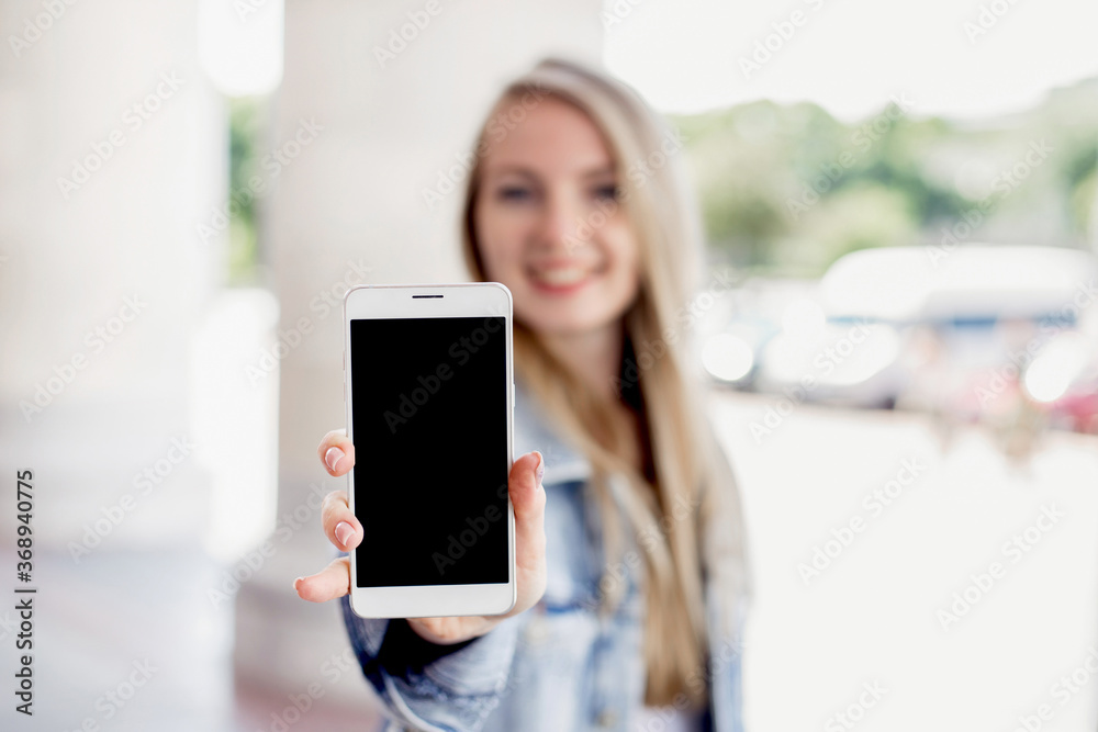 Wall mural close up portrait of female happy smiling student showing a screen of a mobile phone outdoor on the 