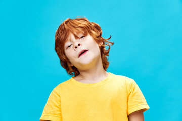 The red-haired boy tilted his head to the side against a blue background