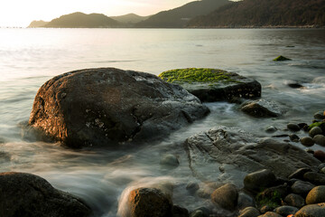 Amazing seashore sunrising,endless horising and green mossy round gravel pebble beach, sea waves beats on a rocky shore with foam.
