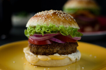 A home-made hamburger is on a bright plate, another is behind it, and a glass of coke is next to it
