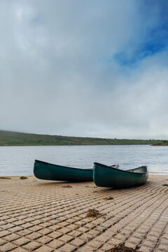 Two blue canoe on rump to water. Nobody. Cloudy sky. Water sports and activity concept. Vertical image.