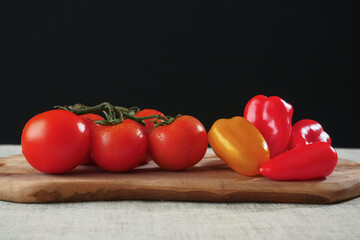 Fresh tomato and red and yellow sweet peppers on a wooden board and simple white table cloth.