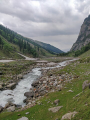 Fototapeta na wymiar Beautiful river stream flowing through rocks in an epic Indian Himalayan Mountain Valley.