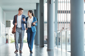 Fototapeta premium Positive young business people walking along airport corridor and discussing work
