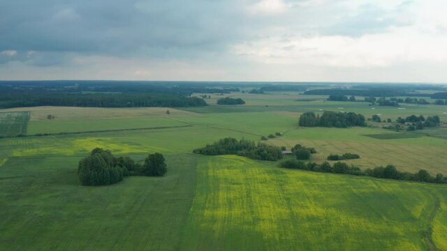 Spectacular landscape flight above green expansive flat plains and farmland in rural countryside on cloudy sky day, Latvia, overhead aerial approach