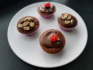 Home-made muffins with chocolate frosting and cherries or salted nuts on a white plate.