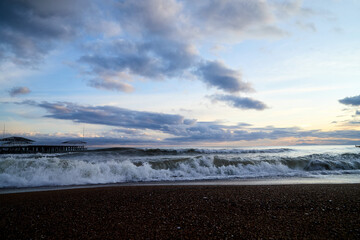 View from beach to water of sea, waves with white foam, pierce and sky with clouds in a nice evening.