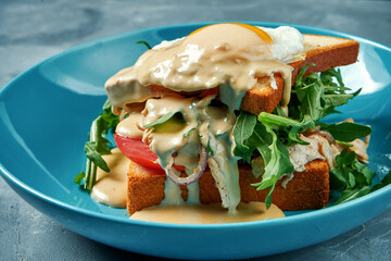 Juicy sandwich with turkey, scrambled eggs and hollandaise sauce in a blue plate