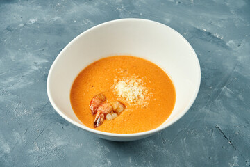 Orange cream soup with salmon and shrimps in a white bowl on a concrete background