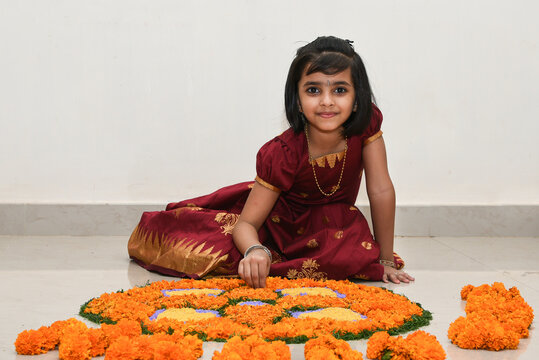 Kerala Onam festival, happy young Indian girl child, wearing traditional dress putting flower bed or Pookalam decoration floral pattern on Onam, Vishu, Diwali celebration, India.  Indian festival.