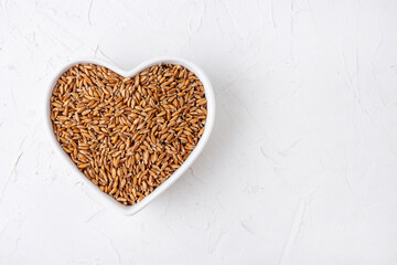spelt in a white heart-shaped plate, on a white table, top view, cereal