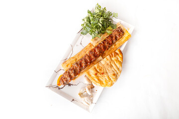 adana kebap.  Turkish Adana Kebab with Vegetables on the Plate.  Traditional oriental Adana kebap and shashlik skewer with tomato and flatbread as top view on a plate with copy space right