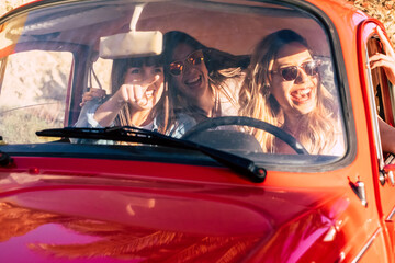 Group of young beautiful women friends inside a red old vintage car enjoy the travel and drive in a...