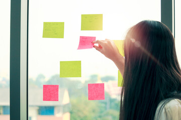 Business woman useing notes to share idea at the meeting room in the office. Sticky paper note on glass wall for brainstorming concept.