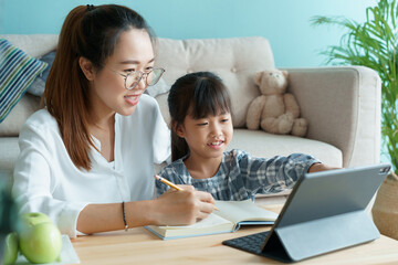 Homeschooling. Asian family with daughter doing homework by using tablet with mother help. 