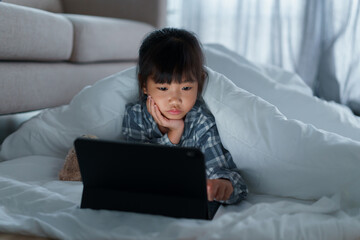 Asian Little girl using tablet digital under blanket in bedroom at night
