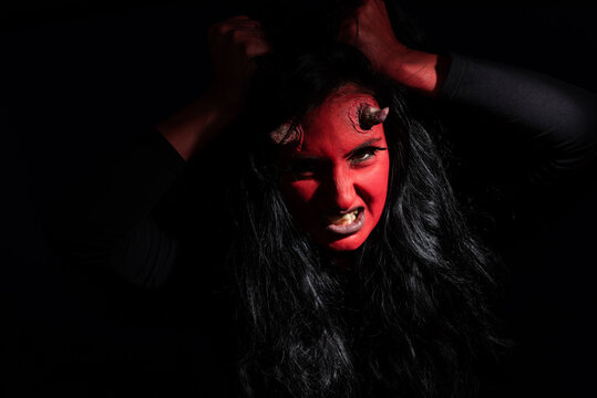 Halloween concept. Demon woman with red face and small horns on black background with copy space. Ideas for halloween body art