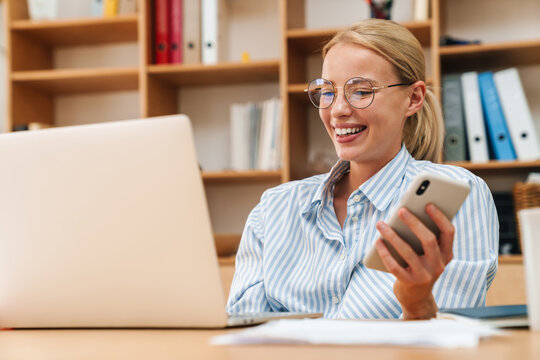 Image of happy woman working with laptop and mobile phone in office