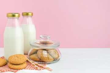 Fresh milk in a glass bottle and oatmeal homemade cookies on a white table with straws on a pink wall background, copy space. Two bottles of healthy natural drink and pastries at summer morning.