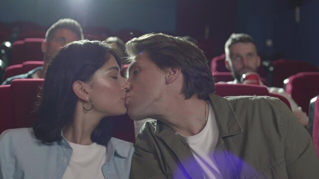 Close up of middle-aged Caucasian couple sitting in cinema and watching film. Then they having a kiss