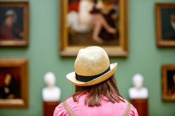 Girl in a hat looks at paintings in a museum - obrazy, fototapety, plakaty