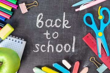 Inscription back to school on the old blackboard with stationery. Colorful crayons, pen, exercise book, scissors,markers and supplies. Chalkboard with pieces of chalk in the classroom.