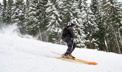 Side view snapshot of skier skiing down the piste along spruce forest. Keeping balance on snow. Concept of extreme winter kinds of sport. Season entertainment