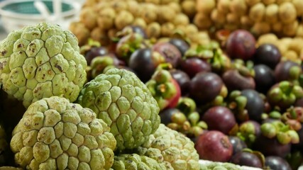Assorted exotic fruits on stall in market. Bunch of sugar apples placed on blurred background of longans and mangosteens on stall on market in tropical country