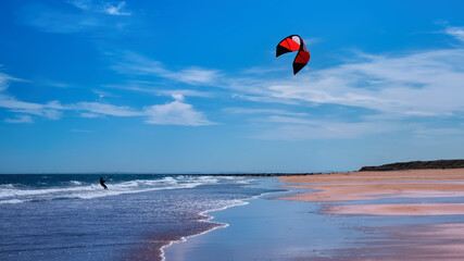 Man kitesurfing or kite boarding sports on Brora beach in the Highlands on a sunny day with blue...