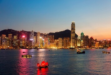 Night scenery of Hong Kong with a skyline of crowded skyscrapers by Victoria Harbor, colorful city lights reflected in the water, ferry boats crossing the seaport and Victoria Peak under twilight sky