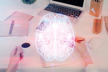 Double exposure of woman's writing hand on background with brain hud. Concept of learning.